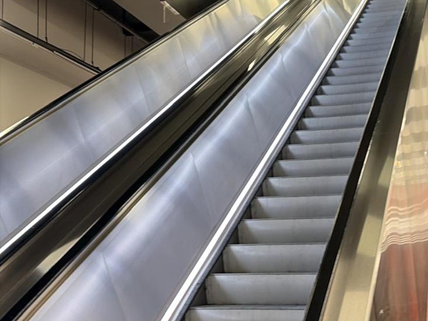 An escalator with stainless-steel balustrades and lit handrails.